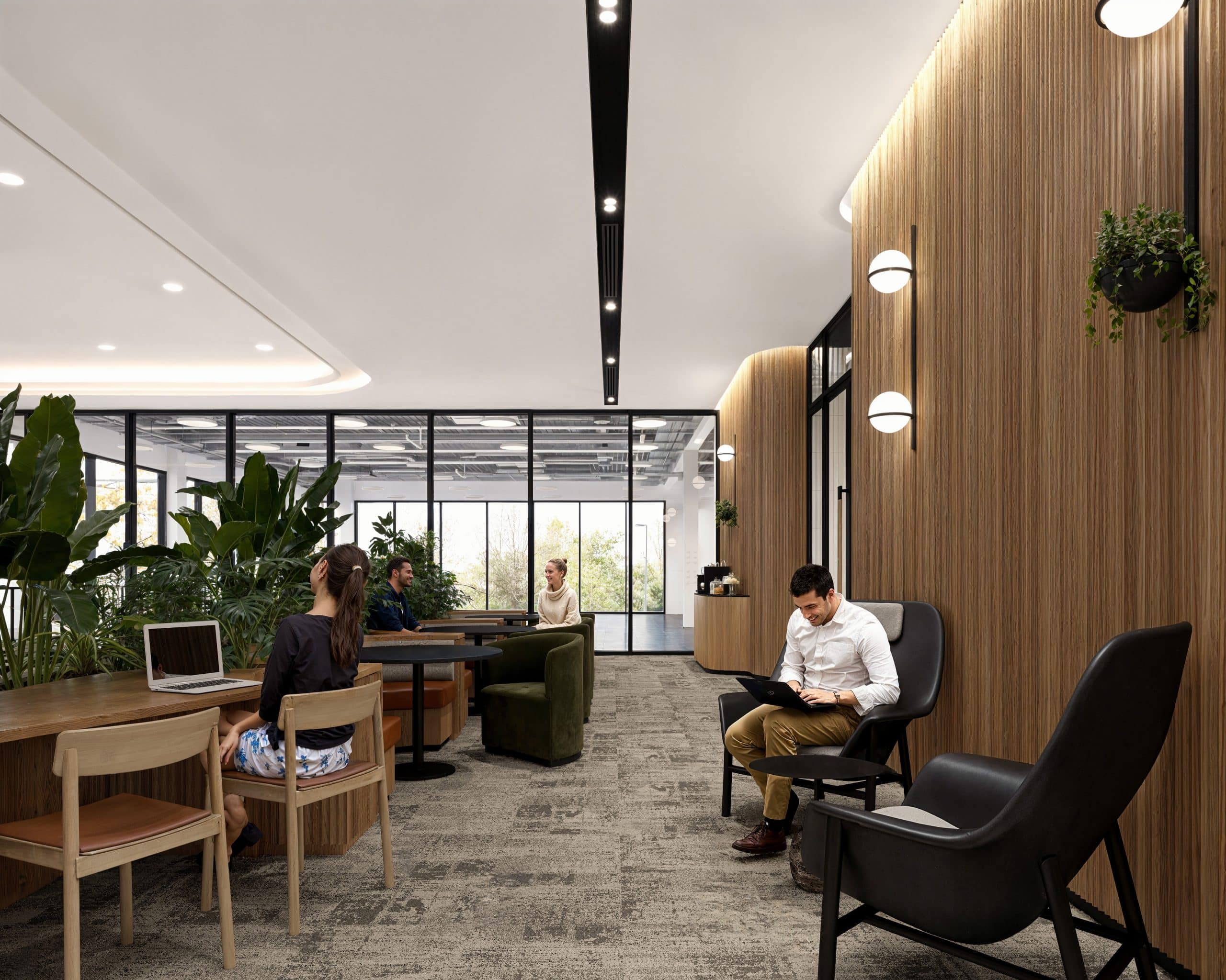 Modern office with plants, people working on laptops, and wooden accents.