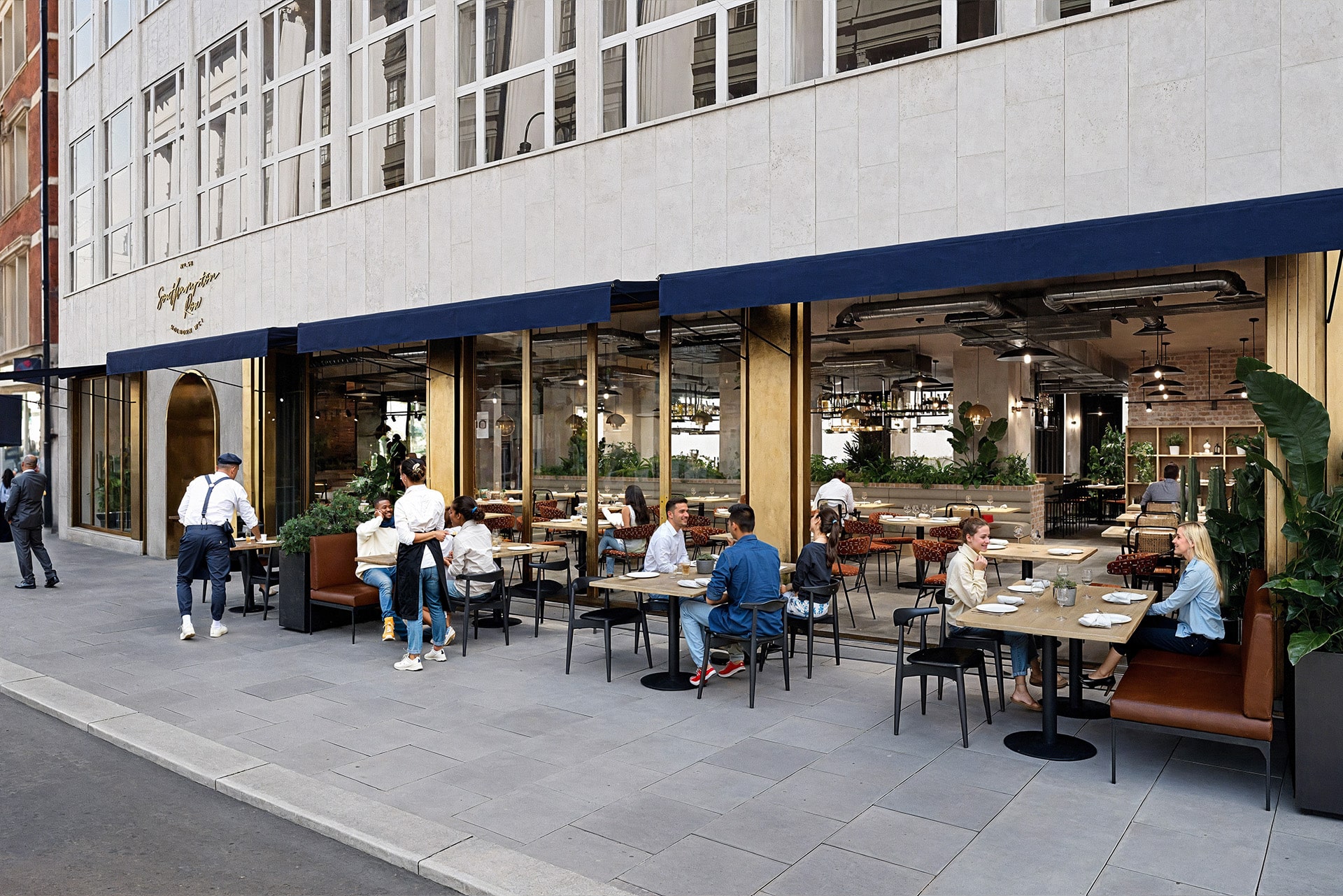 People dining outside a restaurant with blue awnings on a city street.