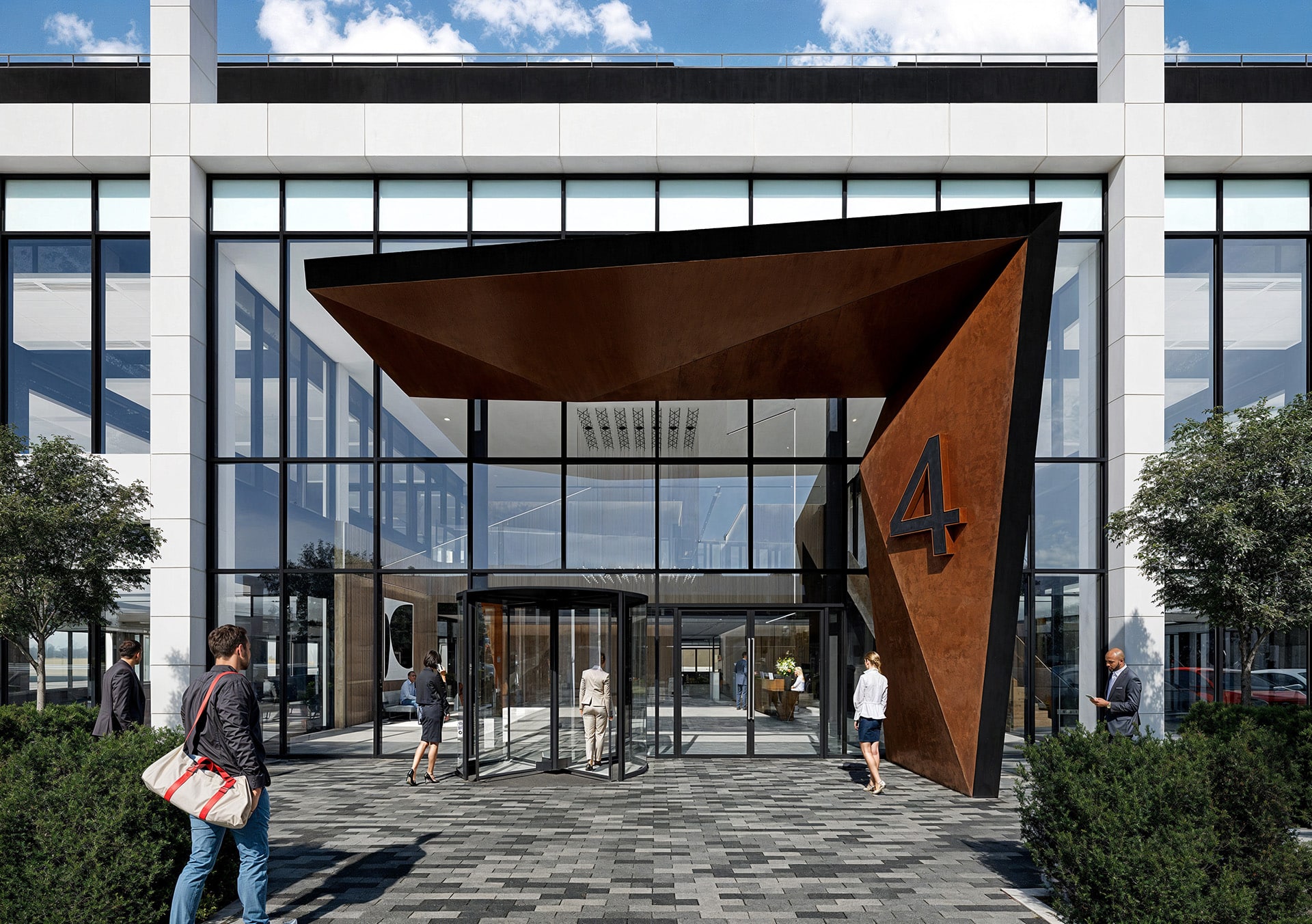 Modern building entrance with angular awning, large glass windows, and people walking nearby.