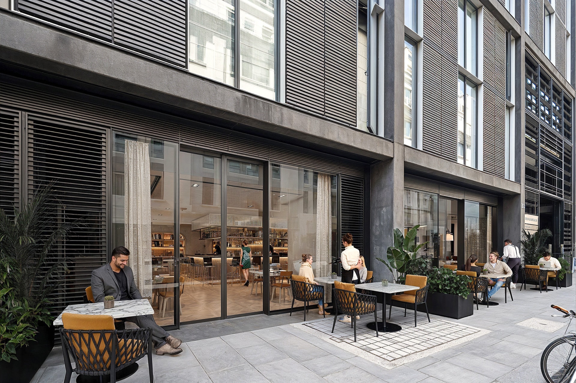 Modern outdoor café with people sitting at tables outside a building with large windows.