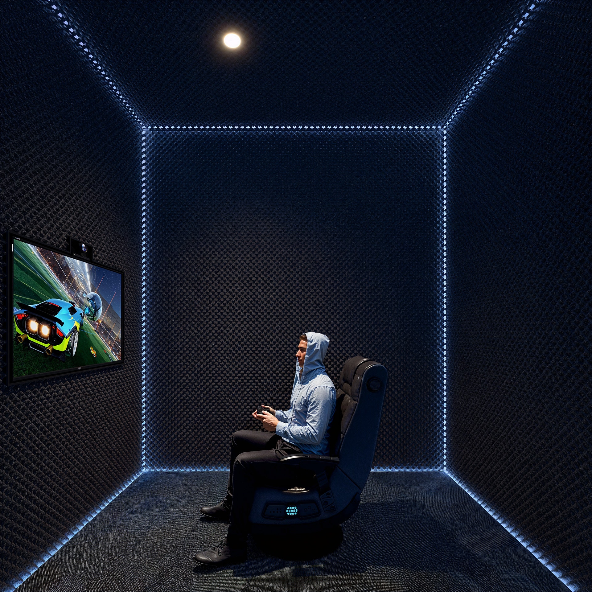 Man playing a video game in a dark, LED-lit room with padded walls.