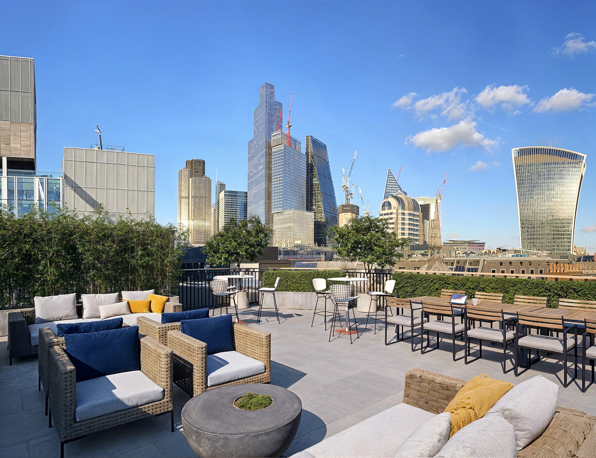 Rooftop lounge with city skyscrapers in the background under a clear blue sky.